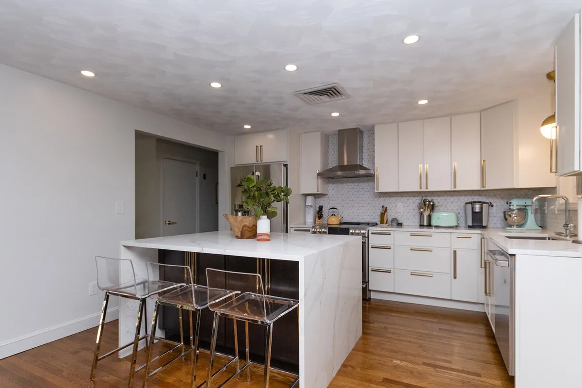 Chestnut Hill kitchen with white cabinets, brass hardware, a marble waterfall island, and hexagon tile backsplash
